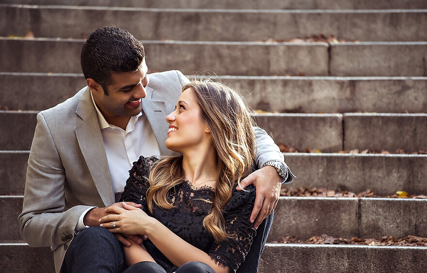 An engaged couple sitting on steps in NYC during the fall.