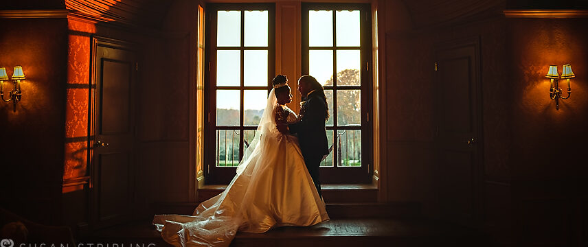 A bride and groom exchanging vows at Oheka Castle, with a window as their stunning backdrop.
