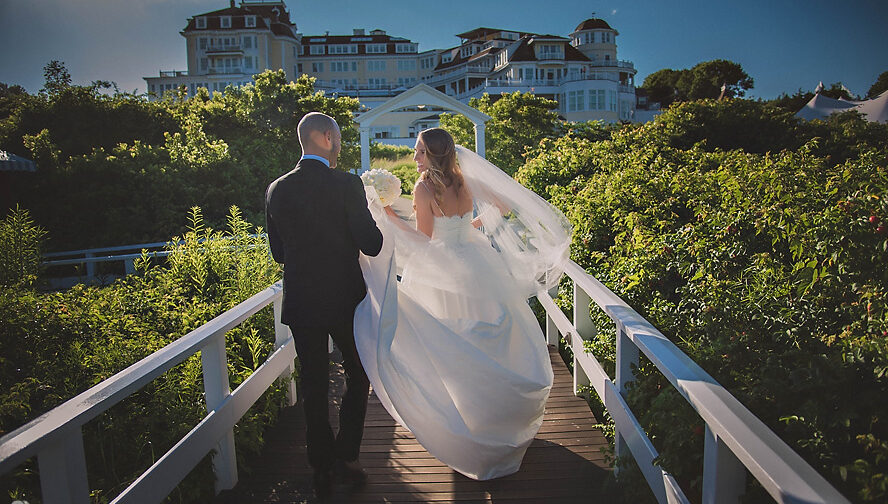 A wedding couple strolling across a bridge in front of a house located in New York City (NYC).