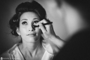 A woman is getting her makeup done in front of a mirror for her wedding in NYC.