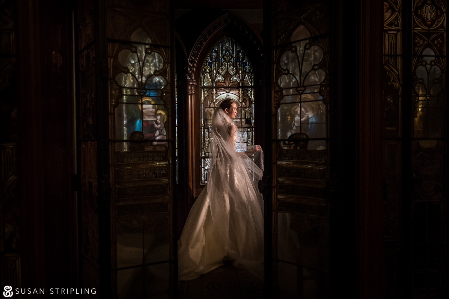 A bride is standing in front of a stained glass window at her wedding in New York City.