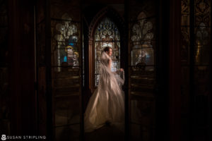 A bride in a wedding dress standing in front of a stained glass window in NYC.