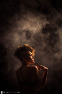 A woman in a black top standing in front of smoke in New York City.