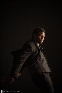 A man in a suit is posing in front of a dark background in New York City.