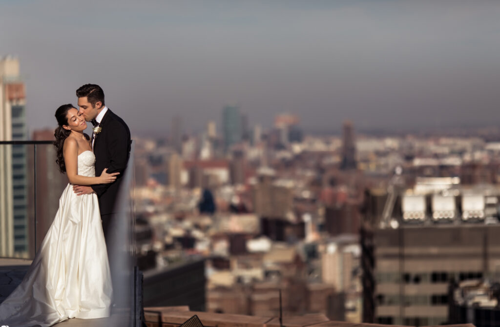 A bride and groom embracing on a rooftop overlooking the city at their Wedding at Chelsea Piers.
