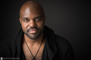 An actor in NYC, dressed in a black shirt, is posing for a headshot photo.