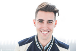 A smiling man wearing a baseball jacket poses for headshots in NYC.