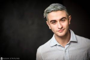 A young man with blue hair posing for a headshot photo.