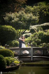 A bride and groom embrace on a bridge in the Brooklyn Botanic Garden during their summer wedding.