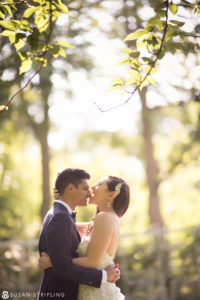 A bride and groom sharing a romantic kiss under the trees at their summer wedding in the Brooklyn Botanic Garden.