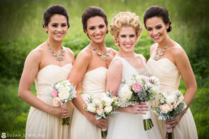 Four bridesmaids holding bouquets in a field during family pictures at a wedding.