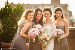 Four bridesmaids pose with their bouquets for family pictures on a rooftop during a wedding.