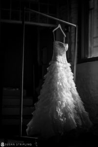 A black and white photo of a wedding dress hanging in a dark room at Angel Orensanz.