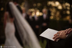 A man is holding a wedding book in front of a bride and groom at an Outdoor Wedding at Oheka Castle.