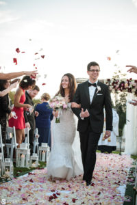 A bride and groom have a breathtaking outdoor wedding at Oheka Castle, walking down the aisle as delicate petals are joyfully thrown at them by their loved ones.