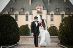 A bride and groom walking in front of Oheka Castle, an outdoor wedding venue.