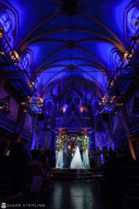 A bride and groom standing in a church lit up with blue lights during their Wedding at Angel Orensanz.
