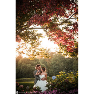 A bride and groom embrace in front of a tree at sunset during their summer wedding at the West Hills Country Club.
