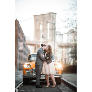 A couple kissing in front of an old car during their Brooklyn winter elopement, with the iconic Brooklyn Bridge as their backdrop.