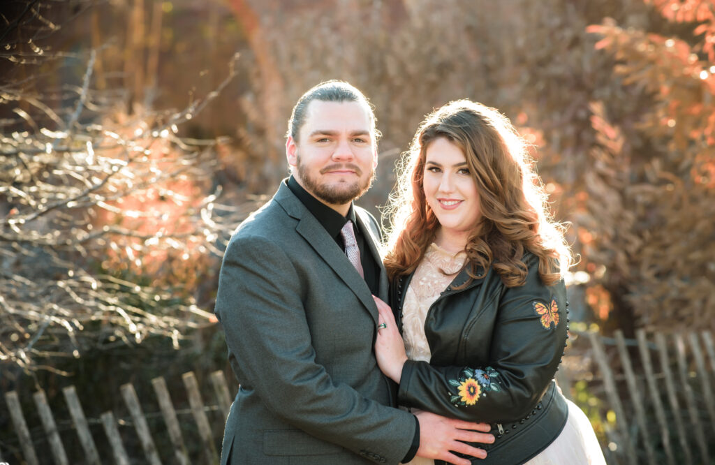 A couple posing for a Brooklyn winter elopement photo in front of a fence.