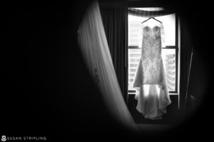 A black and white photo of a wedding dress hanging in a cescaphe window.