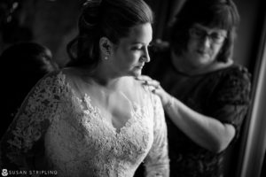 A woman is helping her mother prepare for her Cescaphe Philadelphia wedding by assisting her in putting on her exquisite wedding dress.