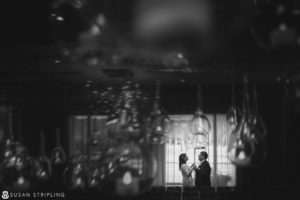 A black and white photo of a bride and groom standing in front of a chandelier at their New Year's Eve wedding.