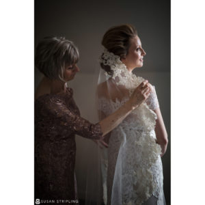 A woman is assisting her mother in wearing her beautiful wedding gown for a destination wedding.
