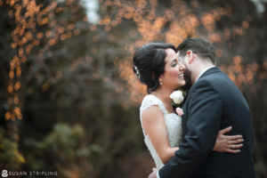 A bride and groom embrace in front of a tree adorned with lights at their wedding at the Madison Hotel.