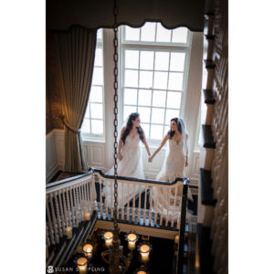 Two brides at Shadowbrook at Shrewsbury standing on a staircase holding hands during their wedding.