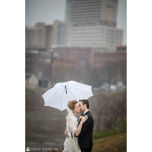 A destination wedding photographer captures the romantic moment of a bride and groom kissing under an umbrella in front of a building.