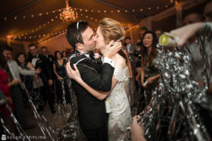 A destination wedding photographer captures a precious moment as a bride and groom kiss amid a shower of confetti.