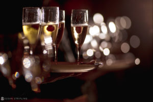 At a rainy day wedding, a person gracefully balances a tray of champagne glasses at Capitale.