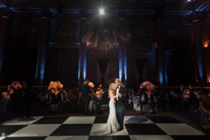 A couple gracefully waltzing on a checkered floor during their rainy day wedding at Capitale.