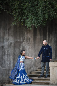 An Indian bride and groom are holding hands on the steps of a stone wall during their wedding in Atlanta.