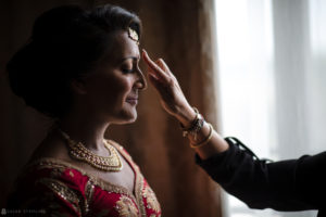 An Indian woman is getting her hair done in preparation for an Atlanta wedding, near a window.