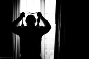 An Indian man adjusting his tie in front of a window during a wedding ceremony in Atlanta.