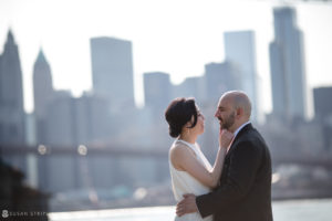 A summer elopement at Brooklyn Bridge Park, with the bride and groom embracing in front of the iconic Brooklyn Bridge.