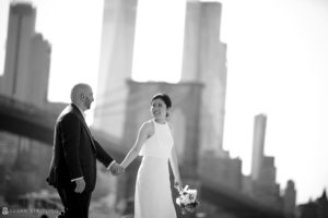 A summer elopement with the bride and groom holding hands in front of the Brooklyn Bridge at Brooklyn Bridge Park.