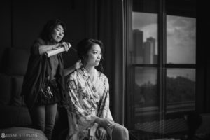 A woman is getting her hair done for her wedding in front of a window at 26 Bridge.