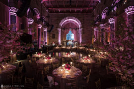 A summer wedding reception at Cipriani 42nd Street, adorned with pink lighting in a large hall.