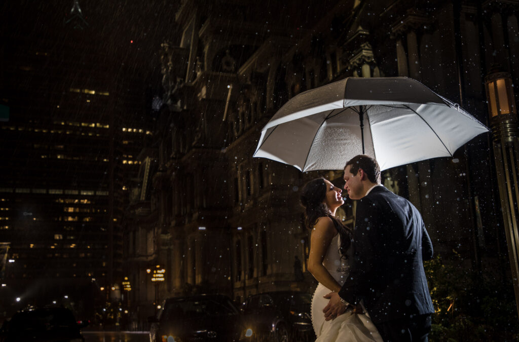 A bride and groom share a romantic kiss under an umbrella in the rain during their wedding at the Crystal Tea Room.