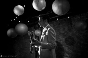 A black and white photo of a man holding a bottle of wine at a wedding at 26 bridge.