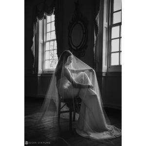 A bride sitting on a chair in front of a window during her wedding at Union Trust in Philadelphia.