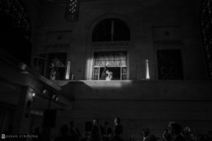 A black and white photo of a bride and groom standing in front of a window at their wedding at Union Trust in Philadelphia.