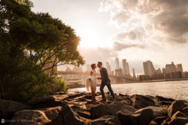 A bride and groom standing on rocks in front of the Brooklyn Bridge, capturing their stunning wedding at 26 Bridge.