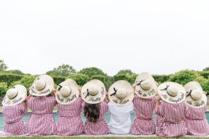 A group of bridesmaids in striped hats sitting by a pool at a Wedding at the Bridgehampton Tennis and Surf Club.