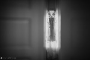 A black and white photo of a wedding dress hanging in a doorway at the Bridgehampton Tennis and Surf Club.
