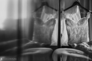 A black and white photo of a wedding dress hanging in a mirror at Flowerfield Celebrations.