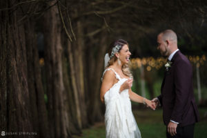 A bride and groom, captured in a picturesque wooded area, exchange vows and hold hands during their wedding ceremony.